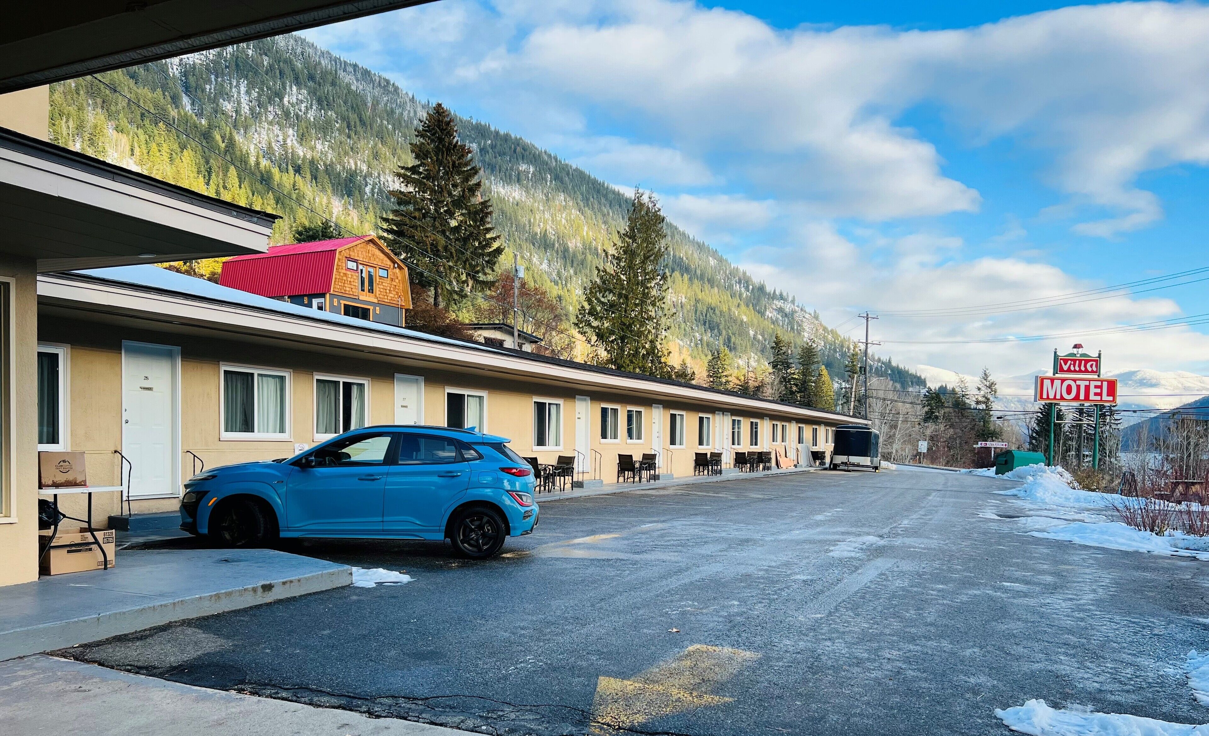 Een motel met een rij kamers, een blauwe auto ervoor geparkeerd, en een berg op de achtergrond.