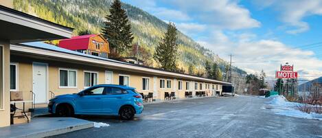 Een motel met een rij kamers, een blauwe auto ervoor geparkeerd, en een berg op de achtergrond.