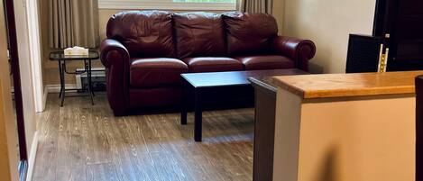 A living room with a brown leather sofa, a small table, and a window with curtains.