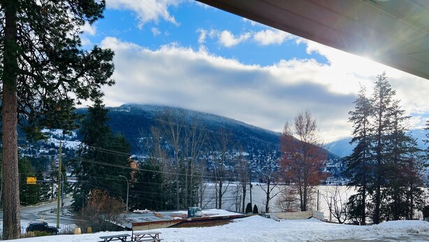 A snowy landscape with a mountain in the background, a road with a fence, and a parked car. - Villa Motel (Nelson)