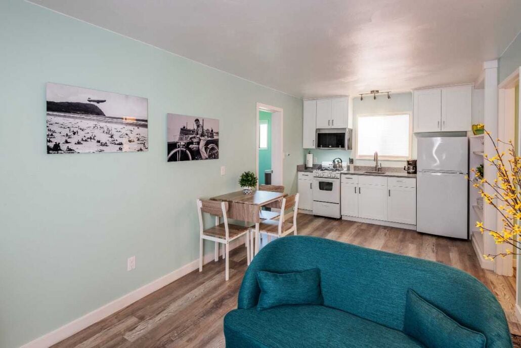 Eine moderne Küche mit weißen Schränken, ein Essbereich mit einem Holztisch und Stühlen sowie zwei gerahmte Bilder an der Wand.