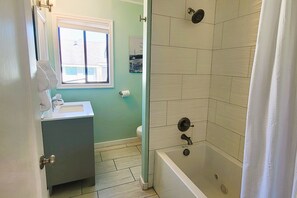 A bathroom with a bathtub, a toilet, and a window.