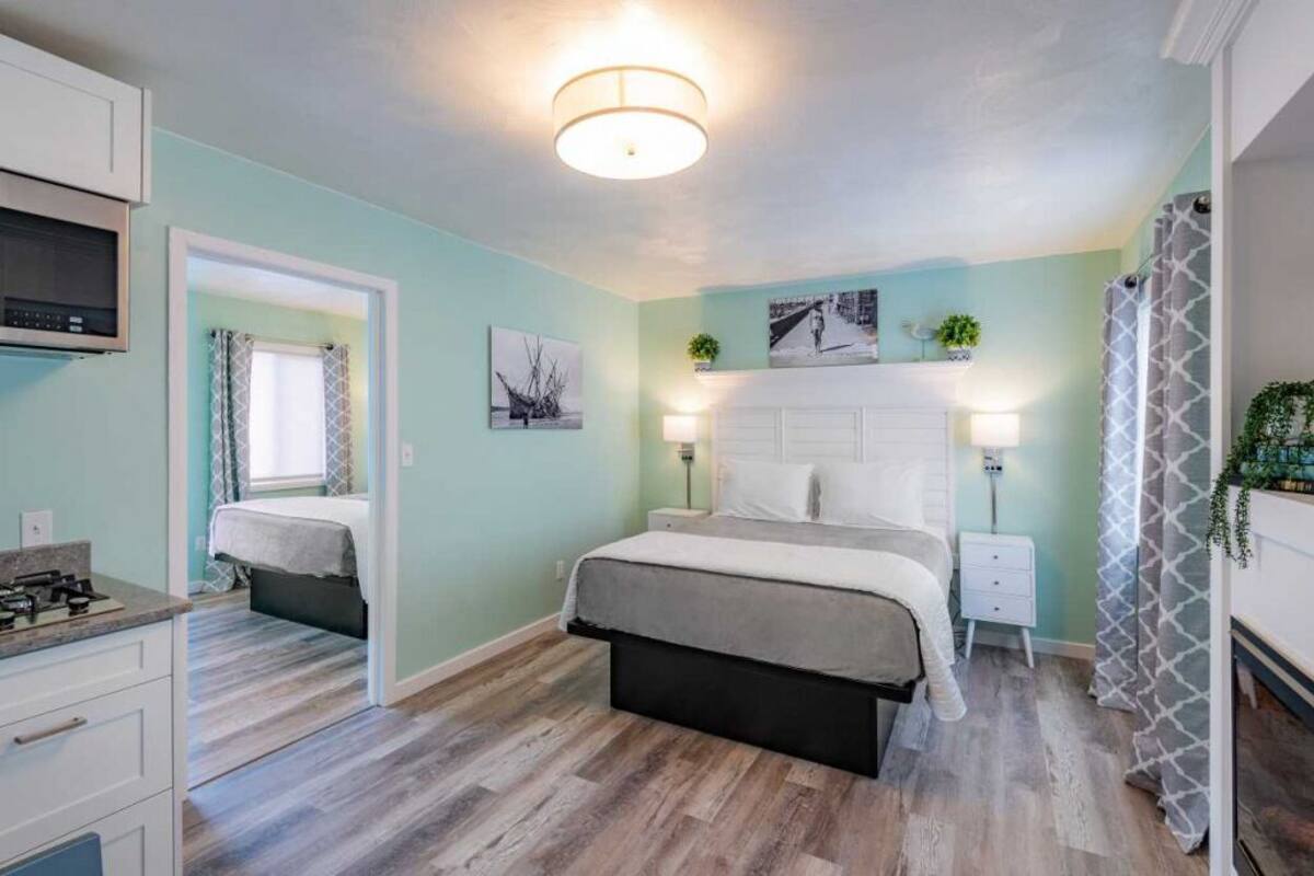 A bedroom with a bed, bedside tables, a nightstand, a ceiling light, a window with curtains, and a wall-mounted TV.