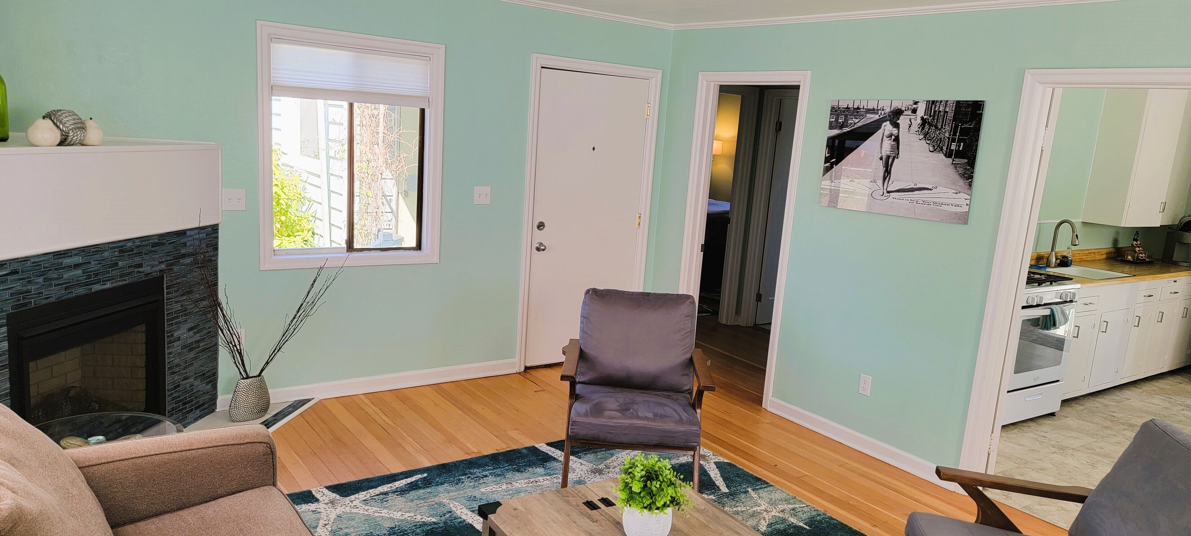 A living room with a fireplace, a sofa, a chair, and a dining area with a kitchen in the background.