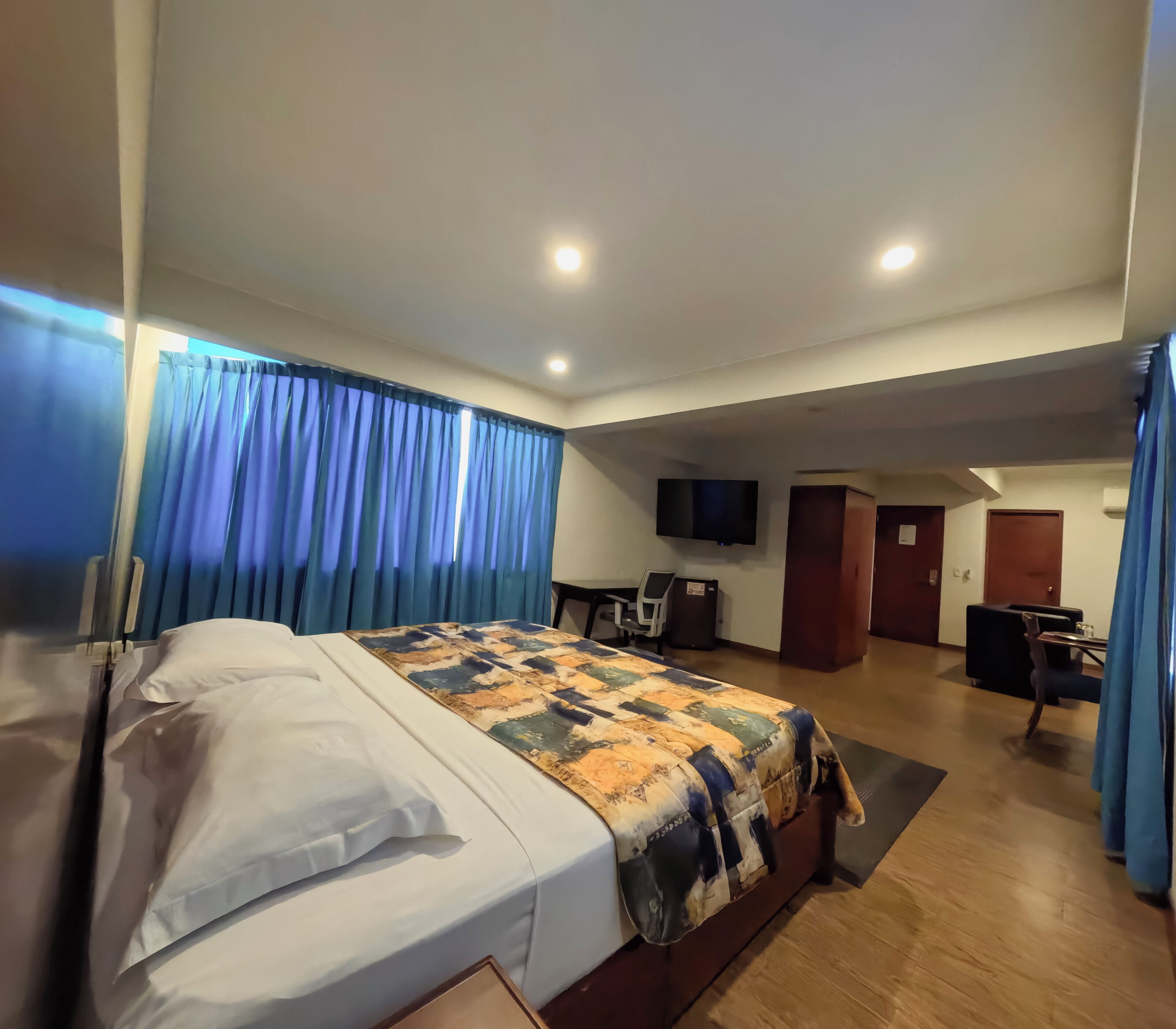 A hotel room with a bed, a desk, a chair, a TV, and a door.