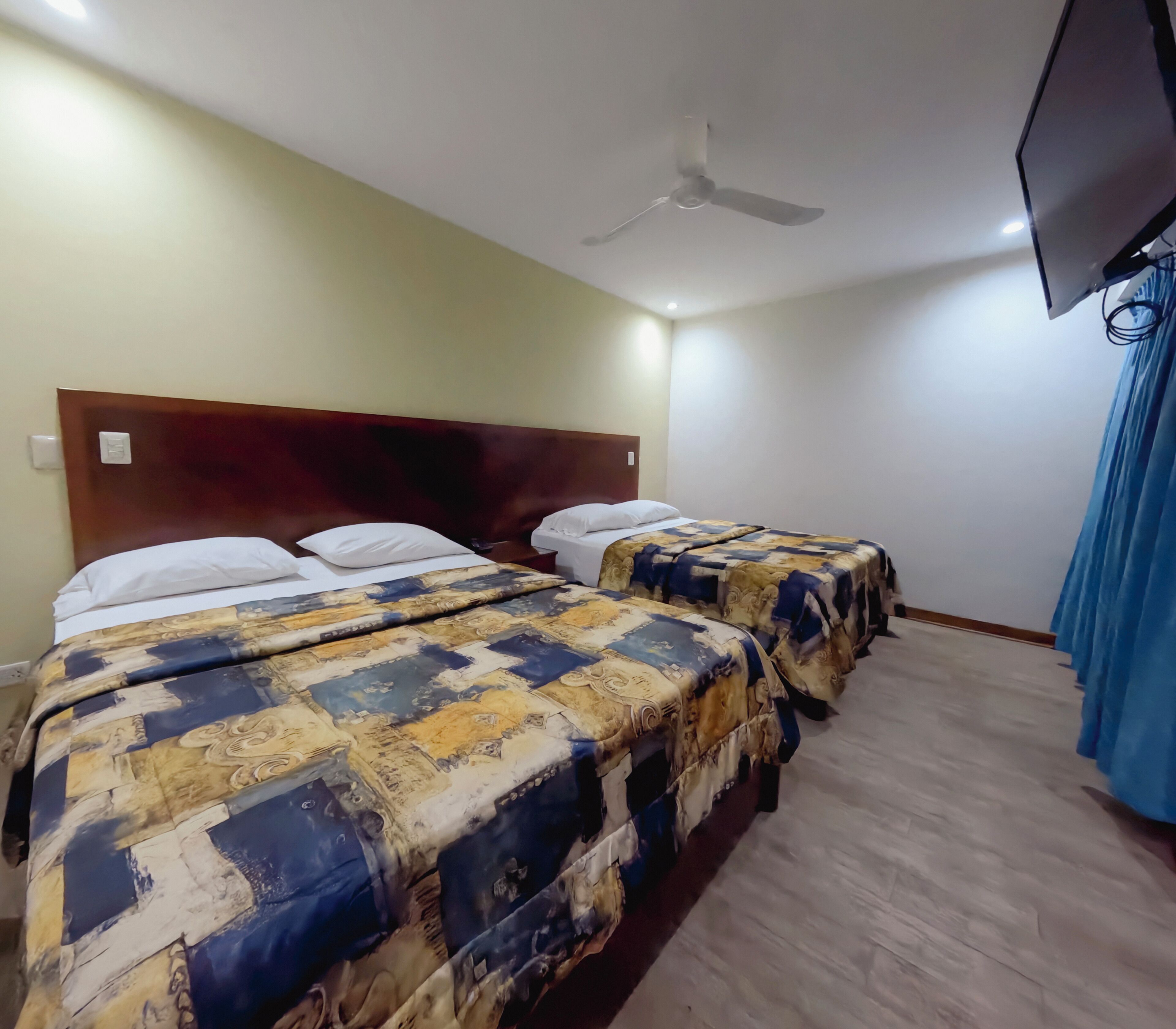 Una habitación de hotel con dos camas, un ventilador de techo y un televisor montado en la pared.