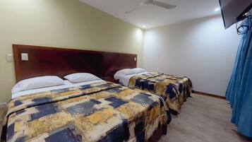 Una habitación de hotel con dos camas, un ventilador de techo y un televisor montado en la pared.