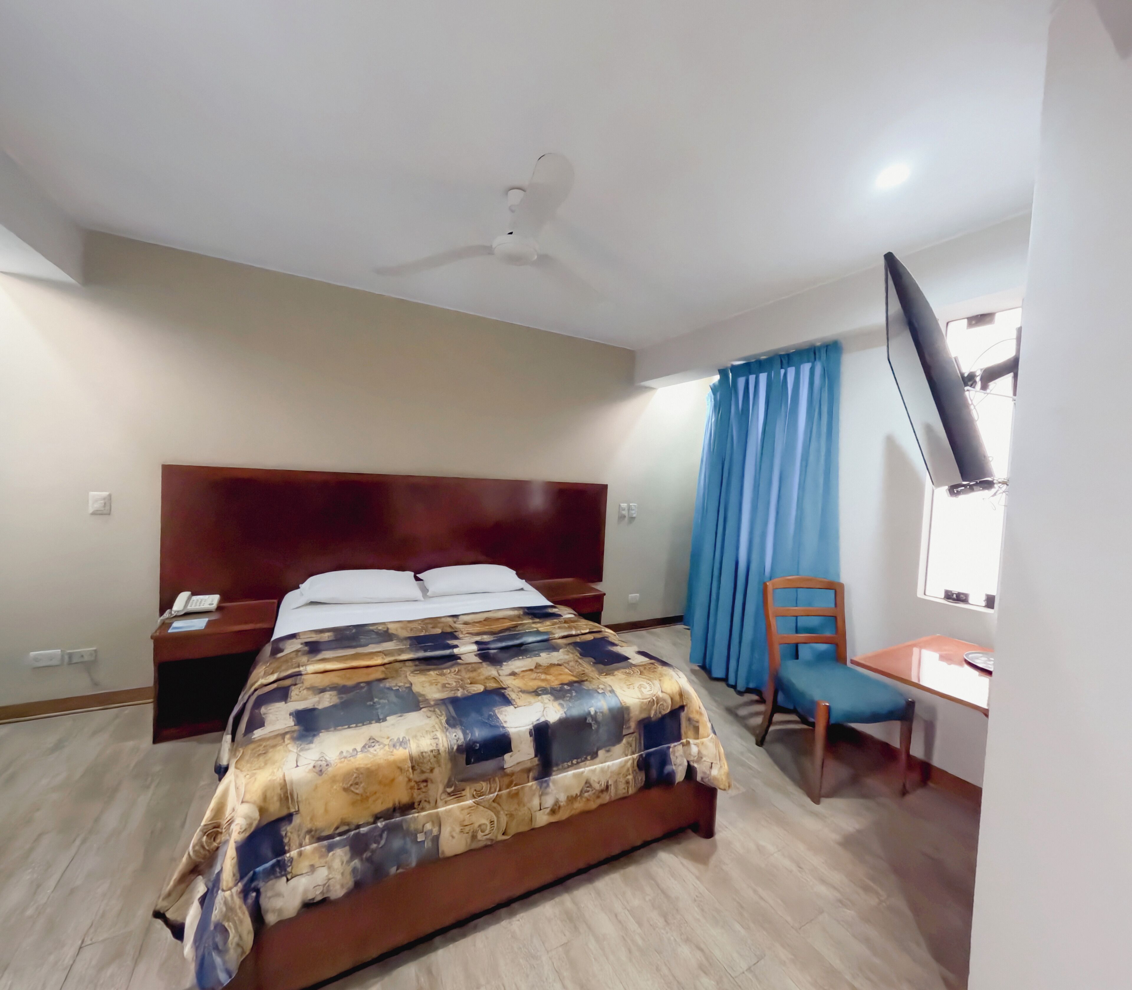 Une chambre d’hôtel équipée d’un lit, d’un bureau, d’une chaise, d’un ventilateur de plafond et d’une télévision.