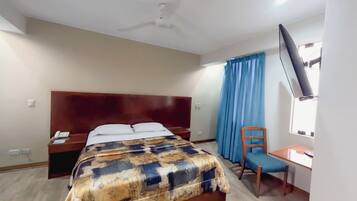 Une chambre d’hôtel équipée d’un lit, d’un bureau, d’une chaise, d’un ventilateur de plafond et d’une télévision.