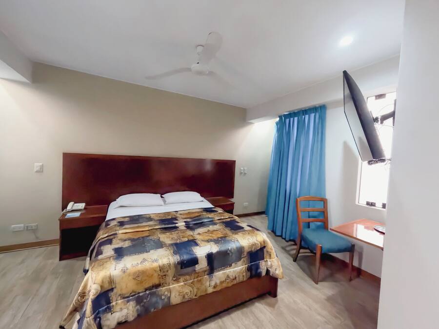Une chambre d’hôtel équipée d’un lit, d’un bureau, d’une chaise, d’un ventilateur de plafond et d’une télévision.