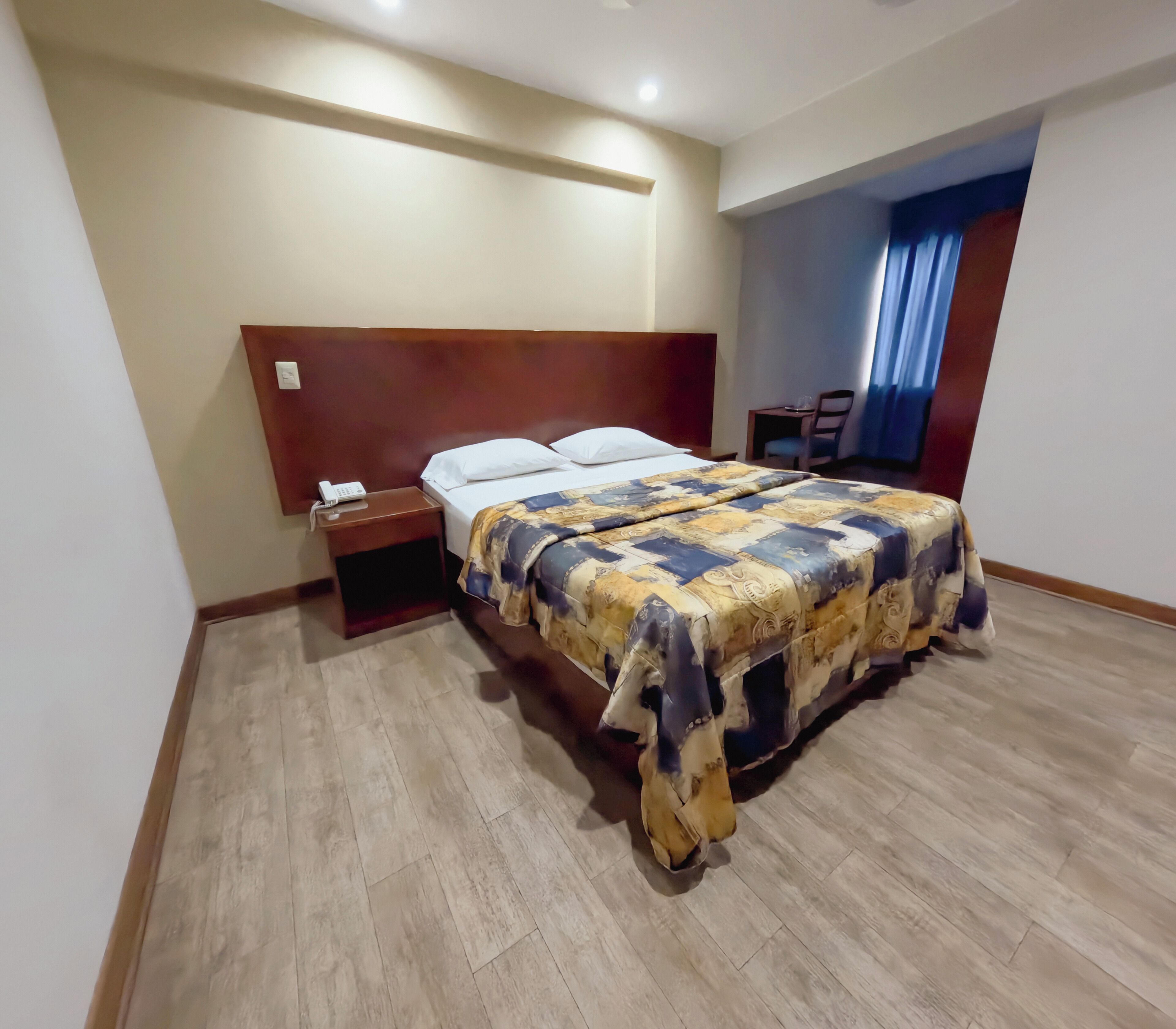 Une chambre d’hôtel comprenant un lit, une table de chevet et un bureau avec une chaise.