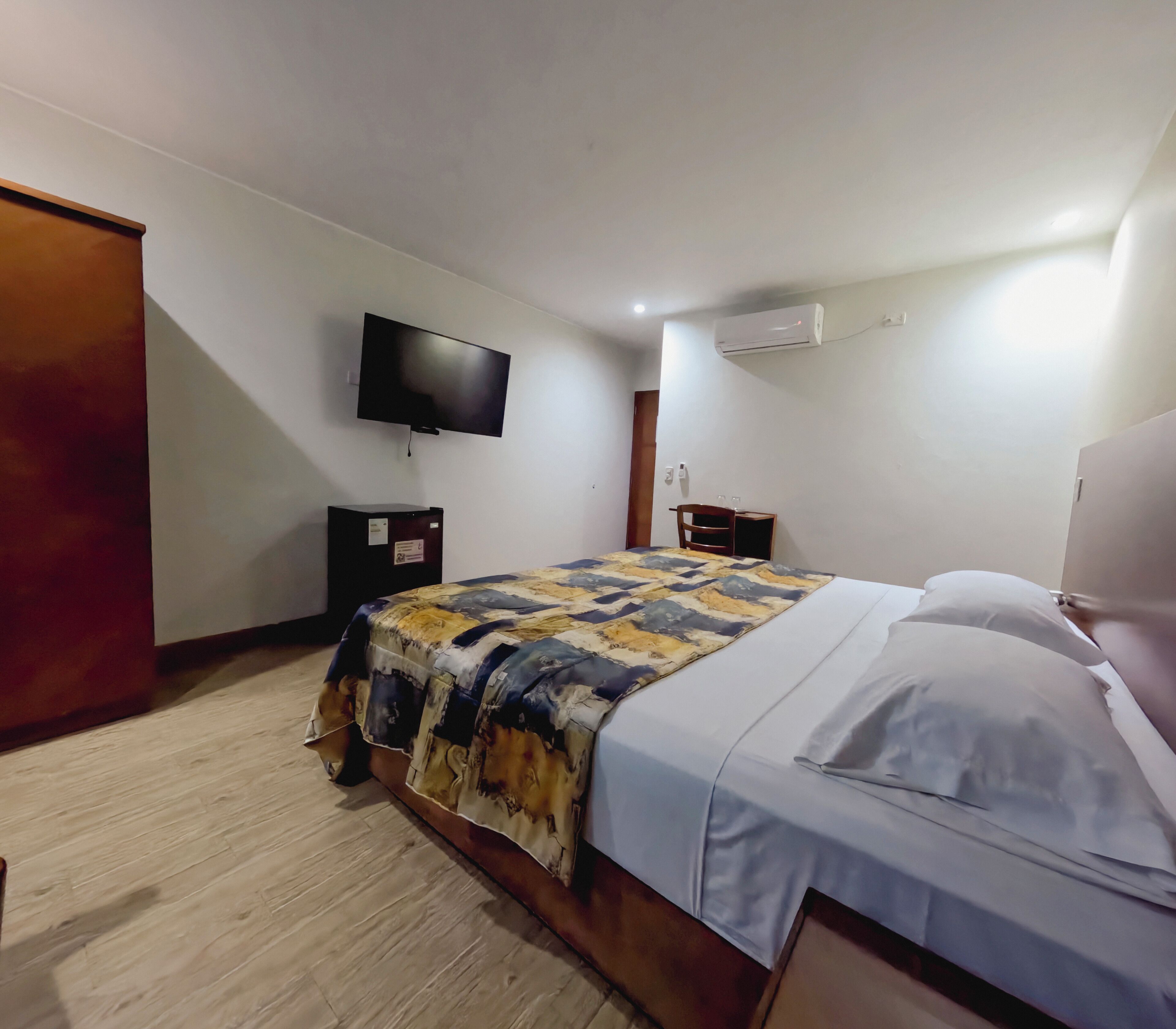 Une chambre à coucher comprenant un lit, un téléviseur fixé au mur, un appareil de climatisation et une armoire.