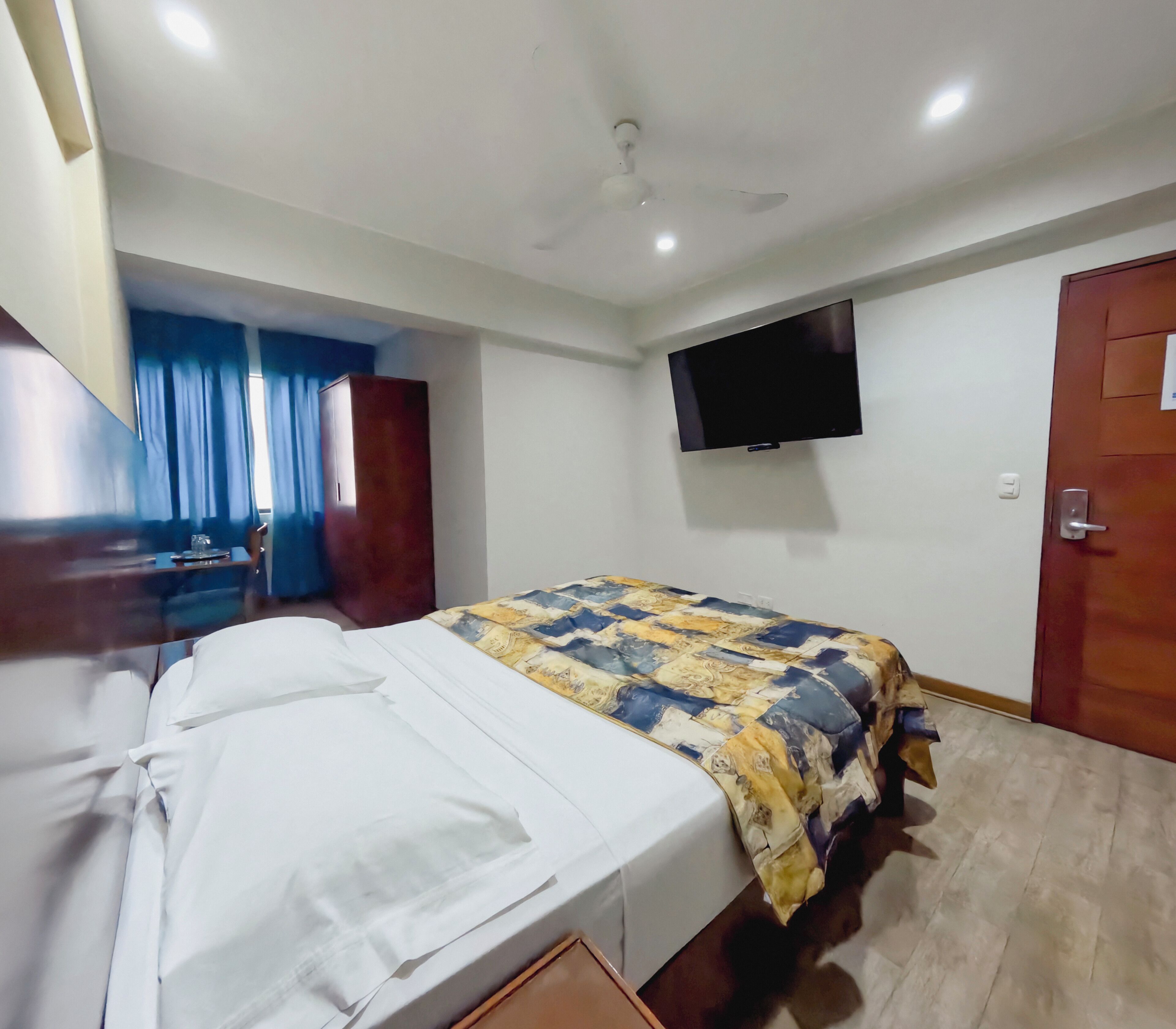 Habitación de hotel con cama, televisor montado en la pared, puerta y ventana con cortinas.