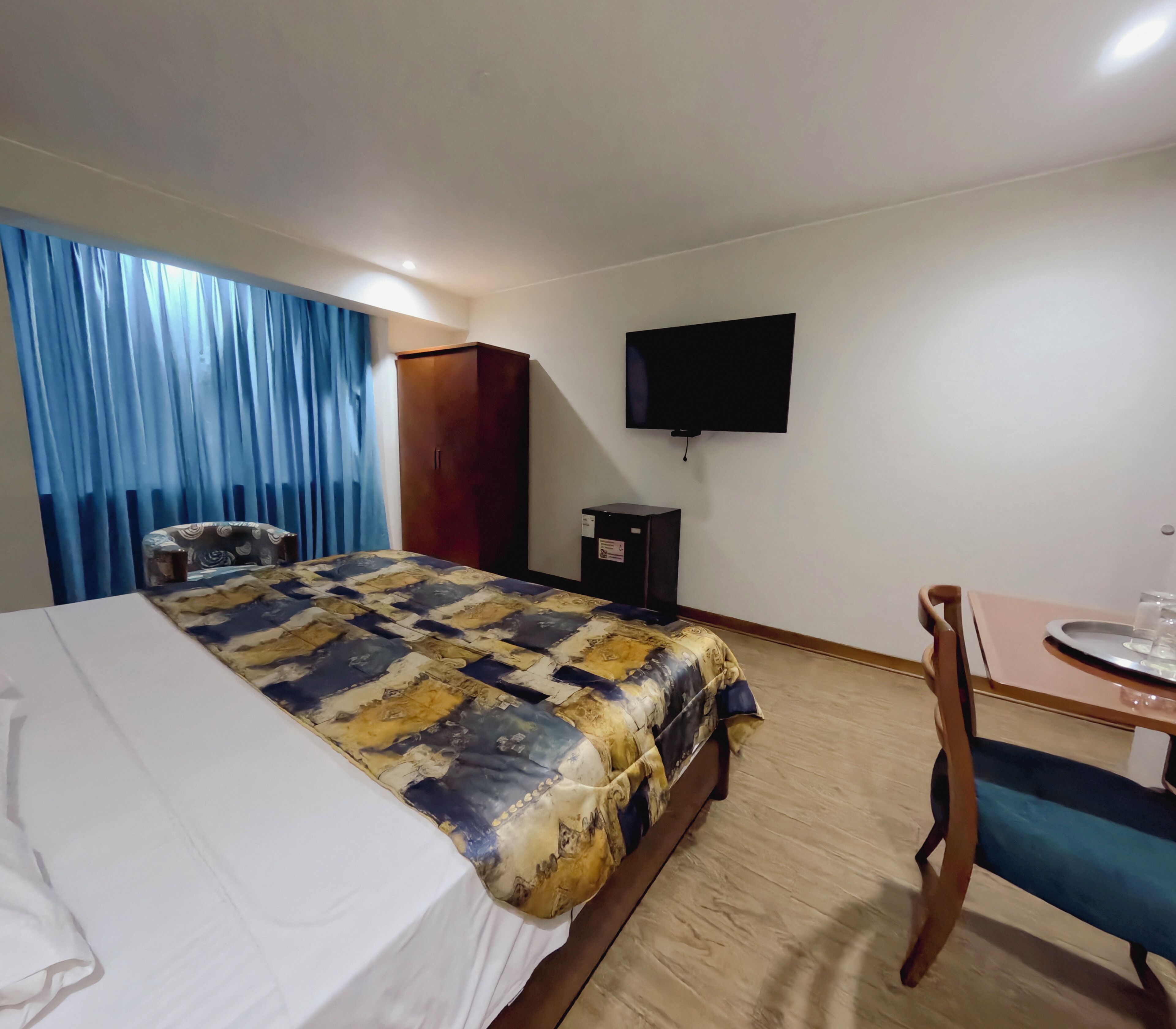 A hotel room with a bed, a desk, a chair, a television, and a wardrobe.