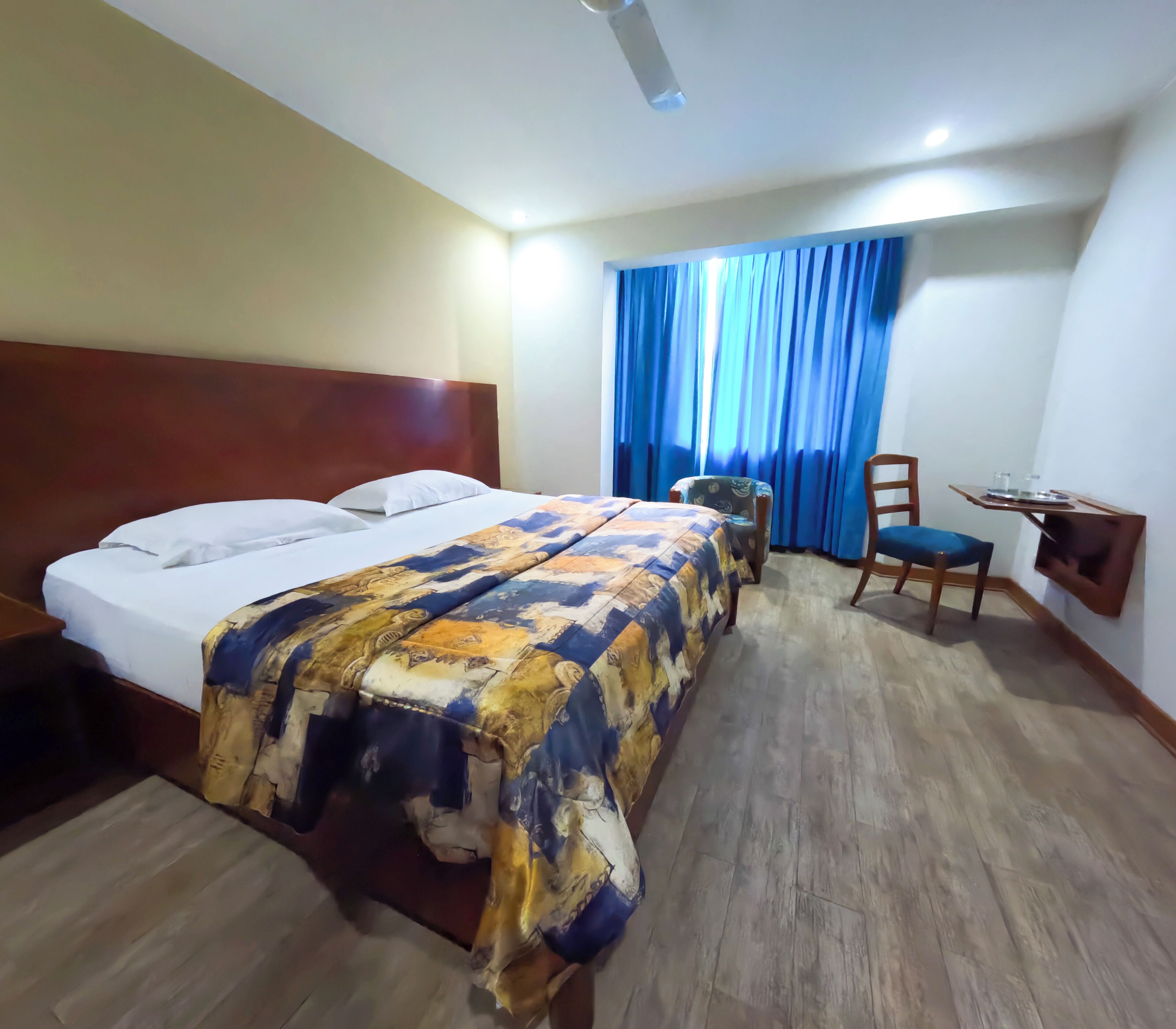 A hotel room with a bed, a chair, a desk, and a window with curtains.