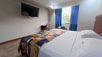 Quarto de hotel com cama, televisão de tela plana na parede, uma mesinha com cadeiras e uma janela com cortinas.