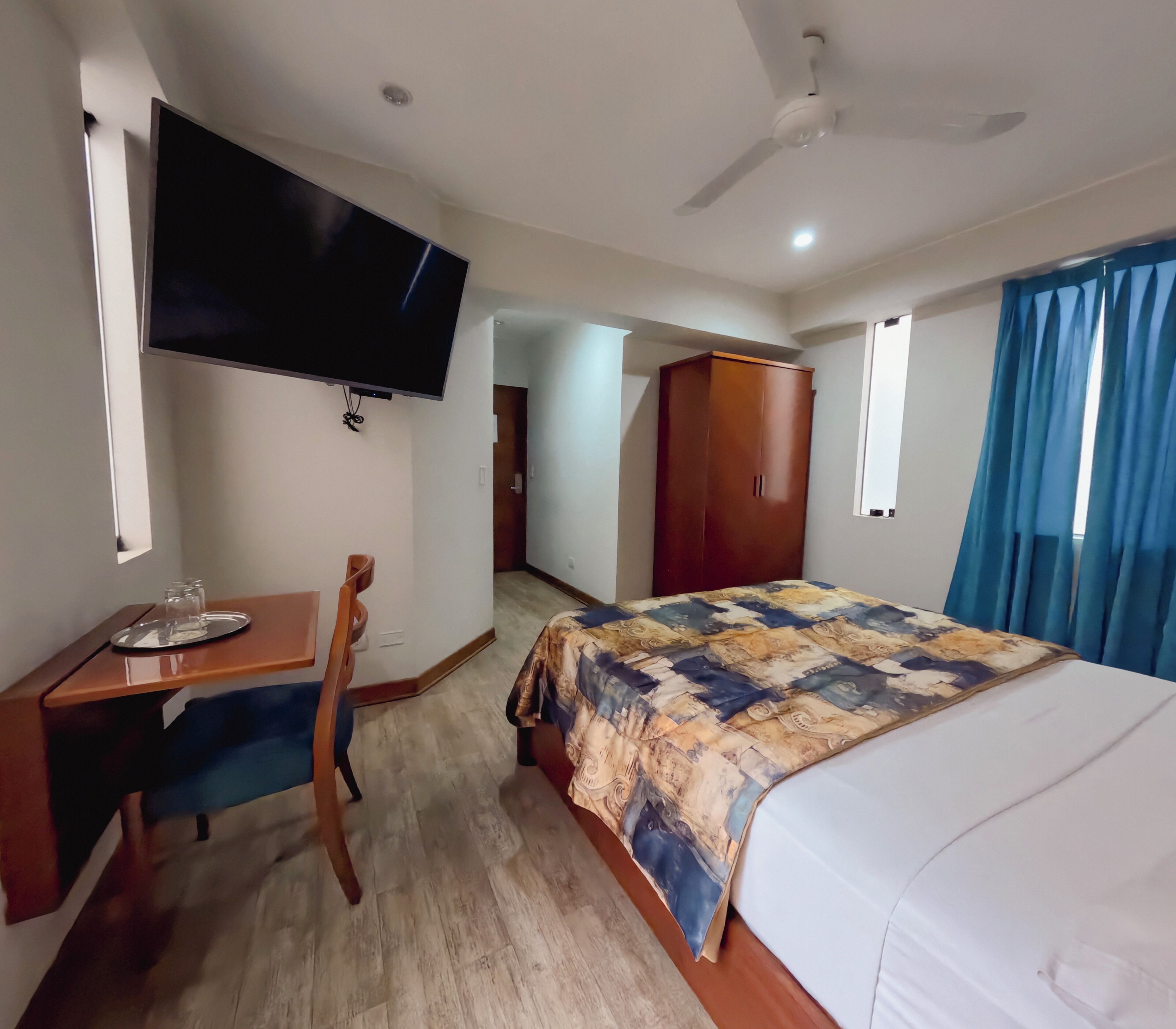 Une chambre d’hôtel comprenant un lit, un bureau avec une chaise, un téléviseur fixé au mur et une armoire.