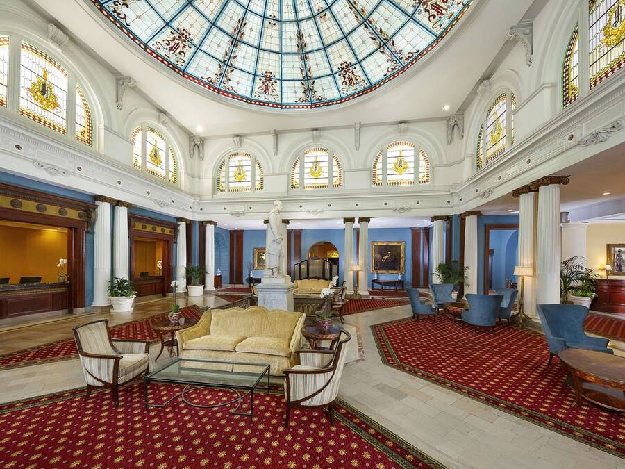 A grand lobby with a high ceiling, ornate columns, and a large stained glass dome.