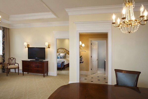 A hotel room with a TV, wooden furniture, a chandelier, and a dining area. - The Jefferson Hotel (Richmond)