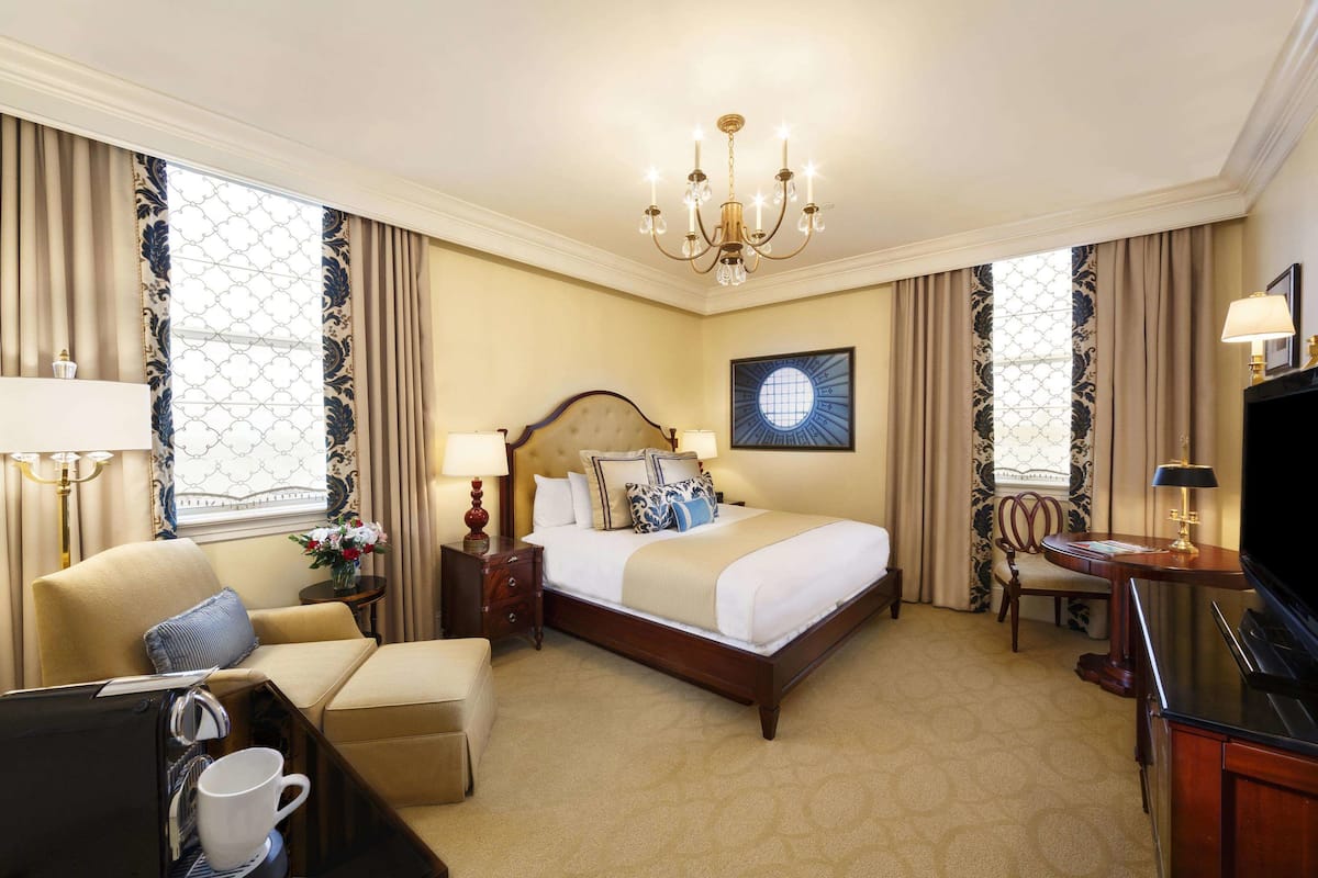 A hotel room with a large bed, a desk, a chair, a coffee table, and a television.
