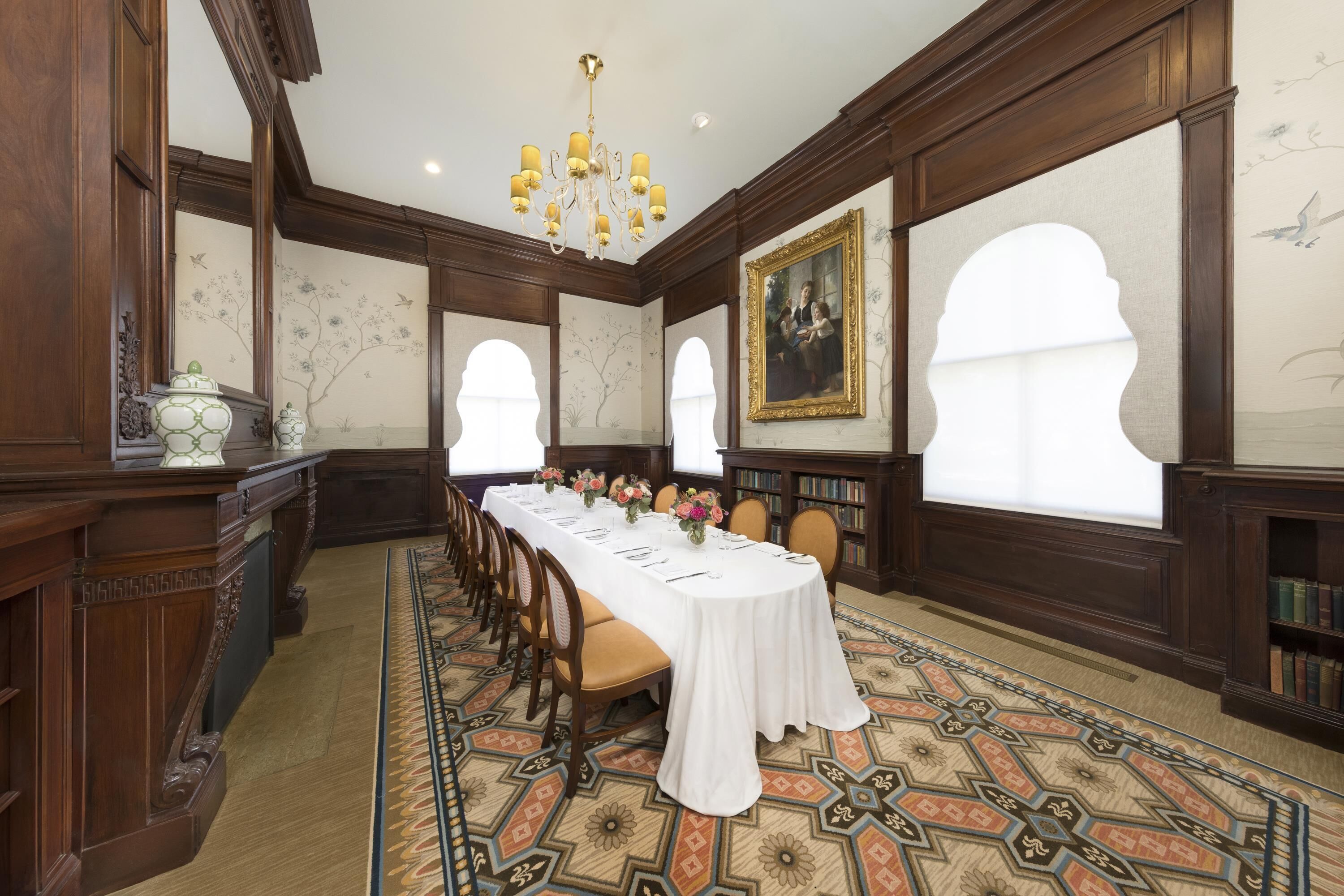A formal meeting room with a long table, chairs, a chandelier, and bookshelves.