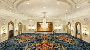 A grand hall with a large, ornate carpet, a chandelier, and a stage with curtains. - The Jefferson Hotel (Richmond)