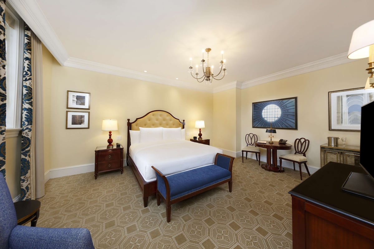 A hotel room with a large bed, two bedside tables with lamps, a desk with a chair, and a television.
