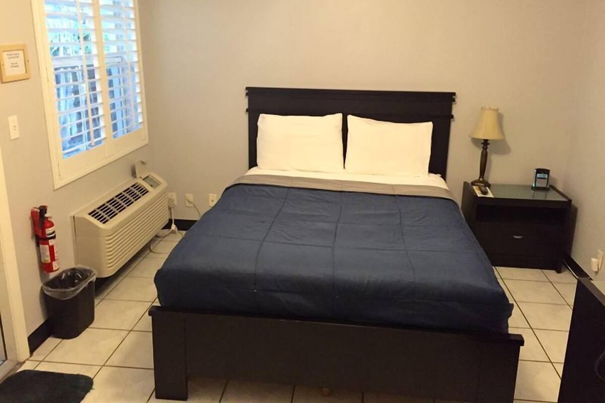 Une chambre à coucher comprenant un lit, une table de chevet, une lampe, un radiateur et une fenêtre avec des stores.