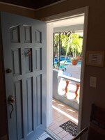 Porta que dá para uma varanda com vista para uma piscina e palmeiras.