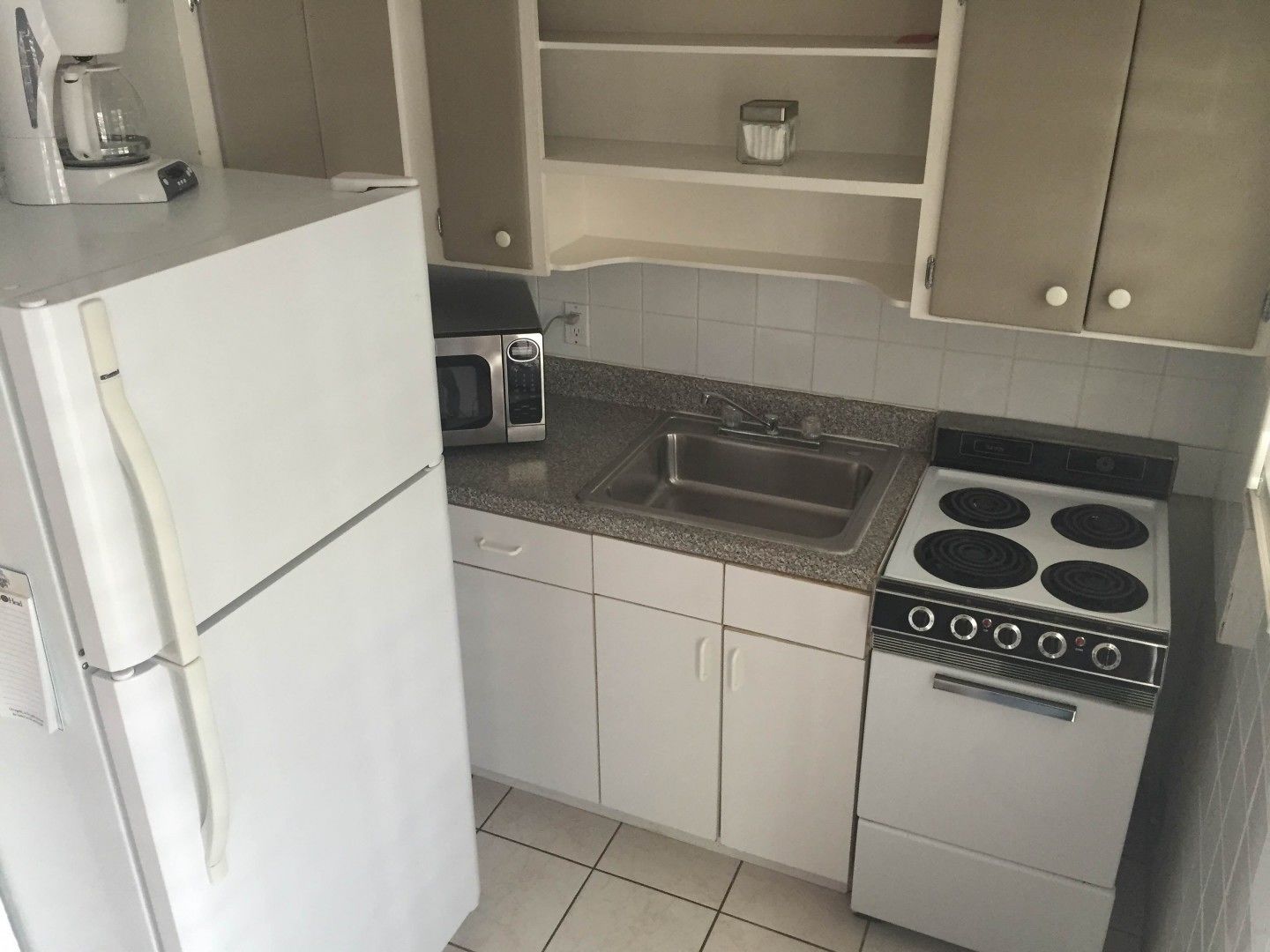 Cocina compacta con refrigerador, microondas, lavamanos y estufa.