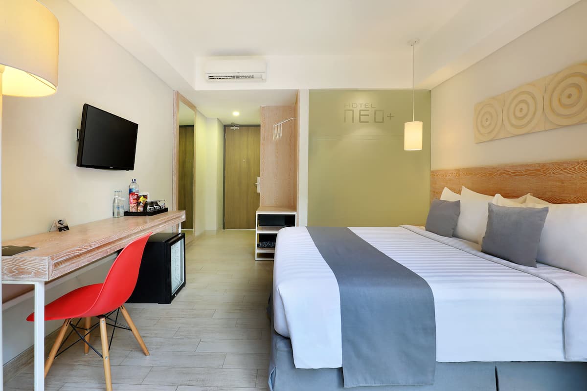 A hotel room with a bed, a desk, a chair, a television, and a shower area.