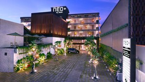Hotel com design moderno, destacando uma placa, um pátio pavimentado com plantas e um carro estacionado na frente.