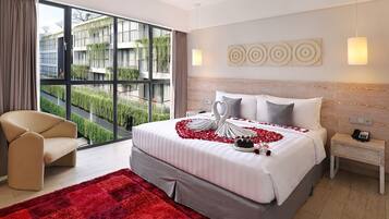 A modern hotel room with a large bed, a view of greenery through floor-to-ceiling windows, a red rug, and a bedside table with a phone.