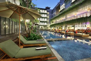 An indoor swimming pool with lounge chairs and umbrellas, surrounded by greenery and modern architecture. - Hotel NEO+ Kuta, Legian by ASTON (Kuta)