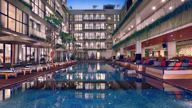 Um átrio de hotel com piscina central, várias varandas e áreas de estar internas.
