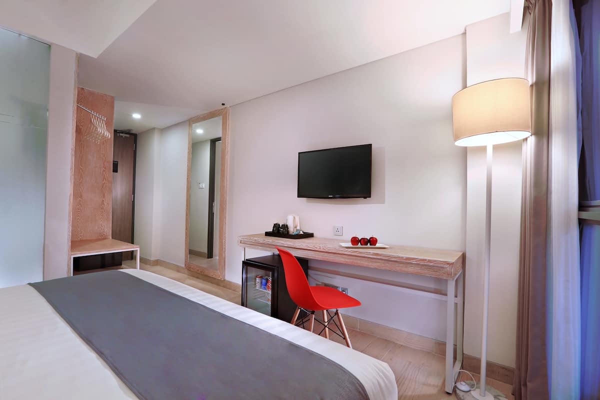 A hotel room with a bed, a desk with a chair, a television, a lamp, and a mirror.