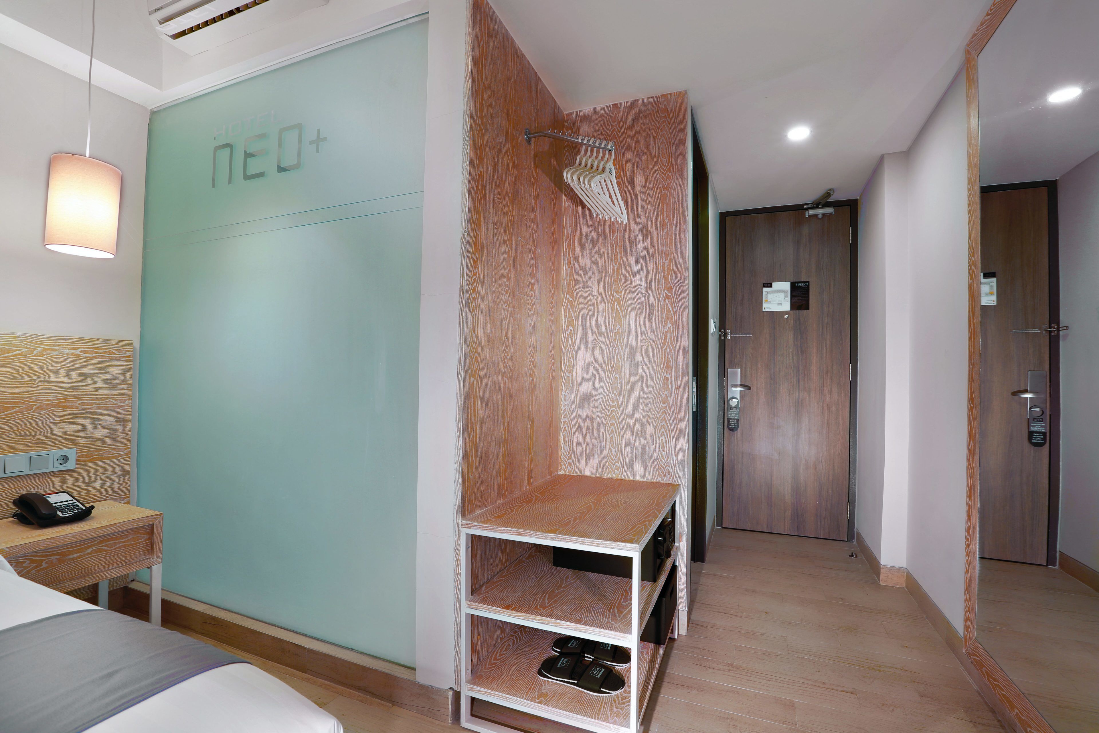 A hotel room with a bed, a desk with a phone, a shoe rack, and a wooden wardrobe.