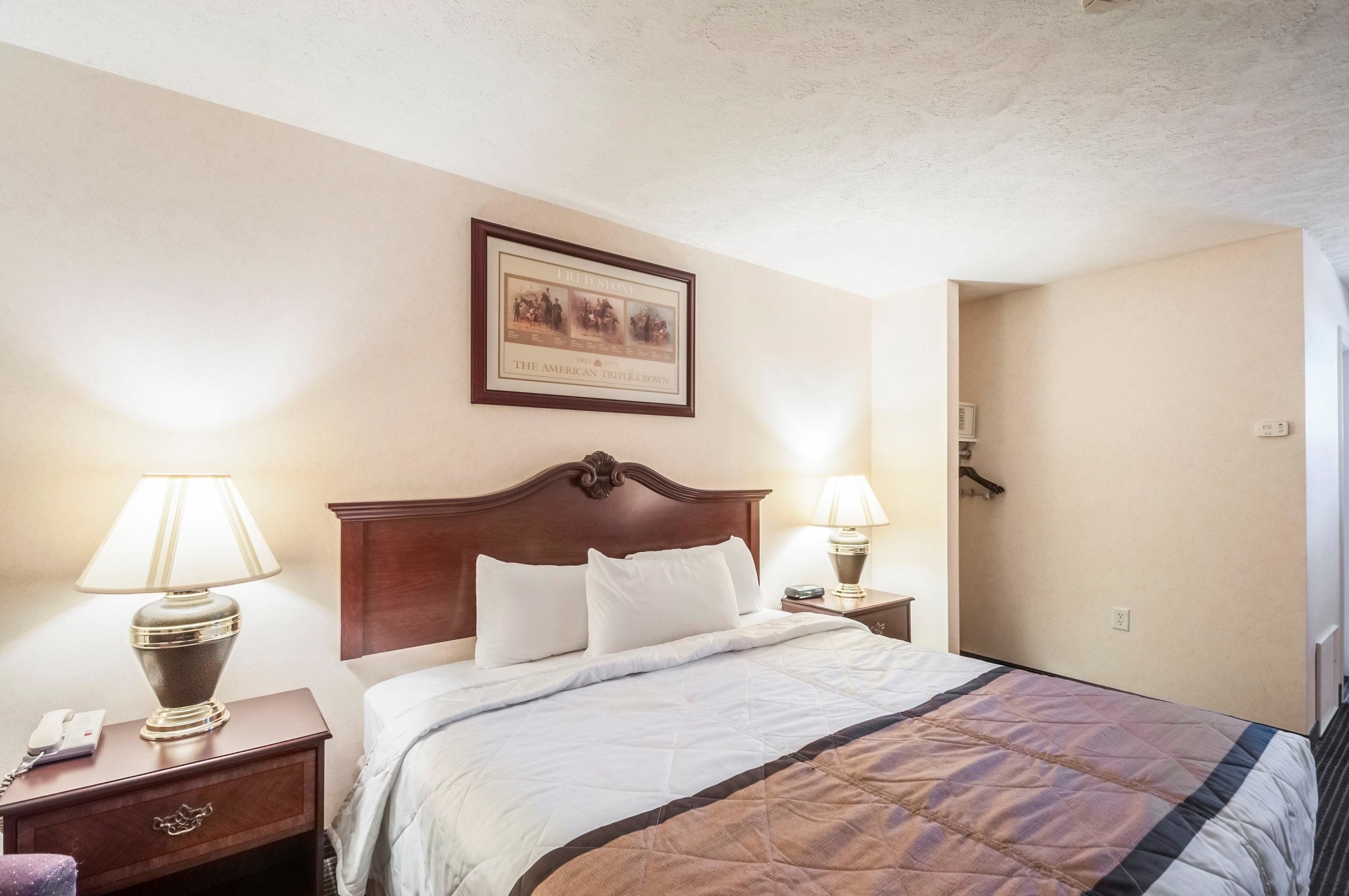 Una cama bien hecha con colcha, dos lámparas de noche, un cuadro en la pared y una mesita de noche de madera con un teléfono.