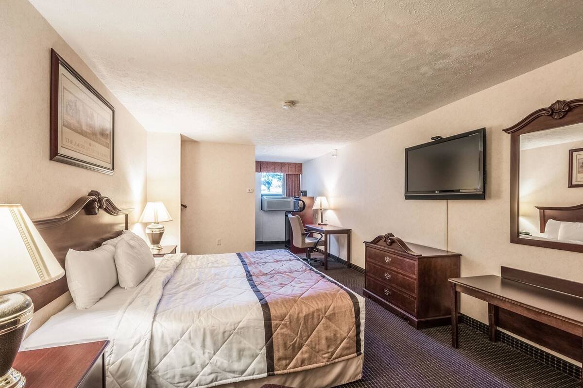 A hotel room with a bed, a desk, a dresser, a TV, and a window.