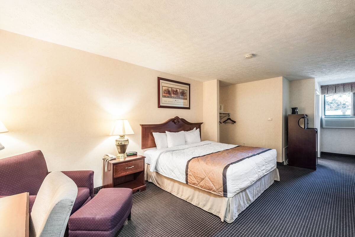 A hotel room with a bed, a nightstand, a chair, a desk, and a window.