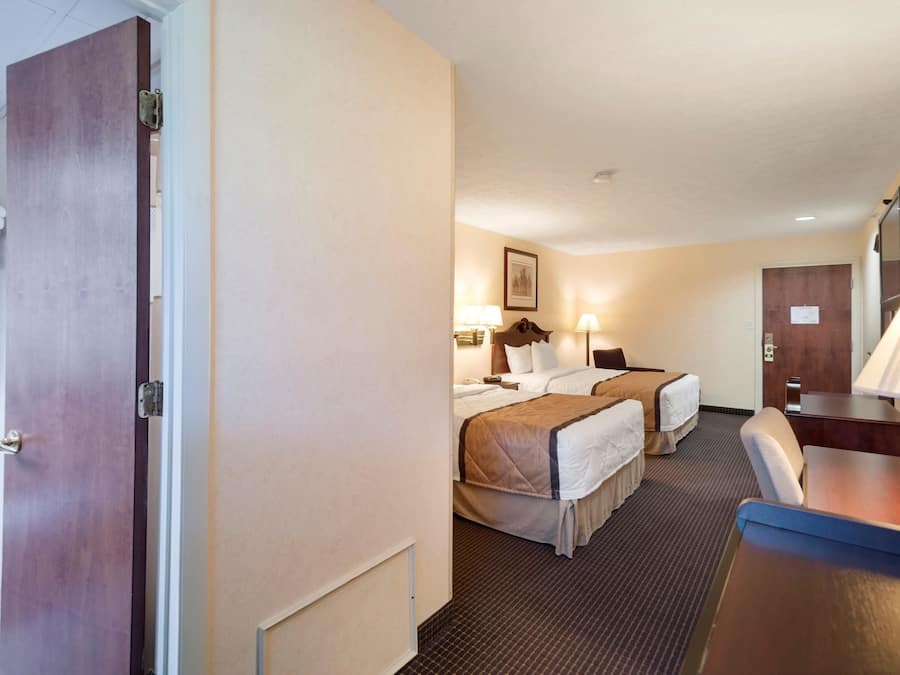 A hotel room with two beds, a desk, a chair, and a television.