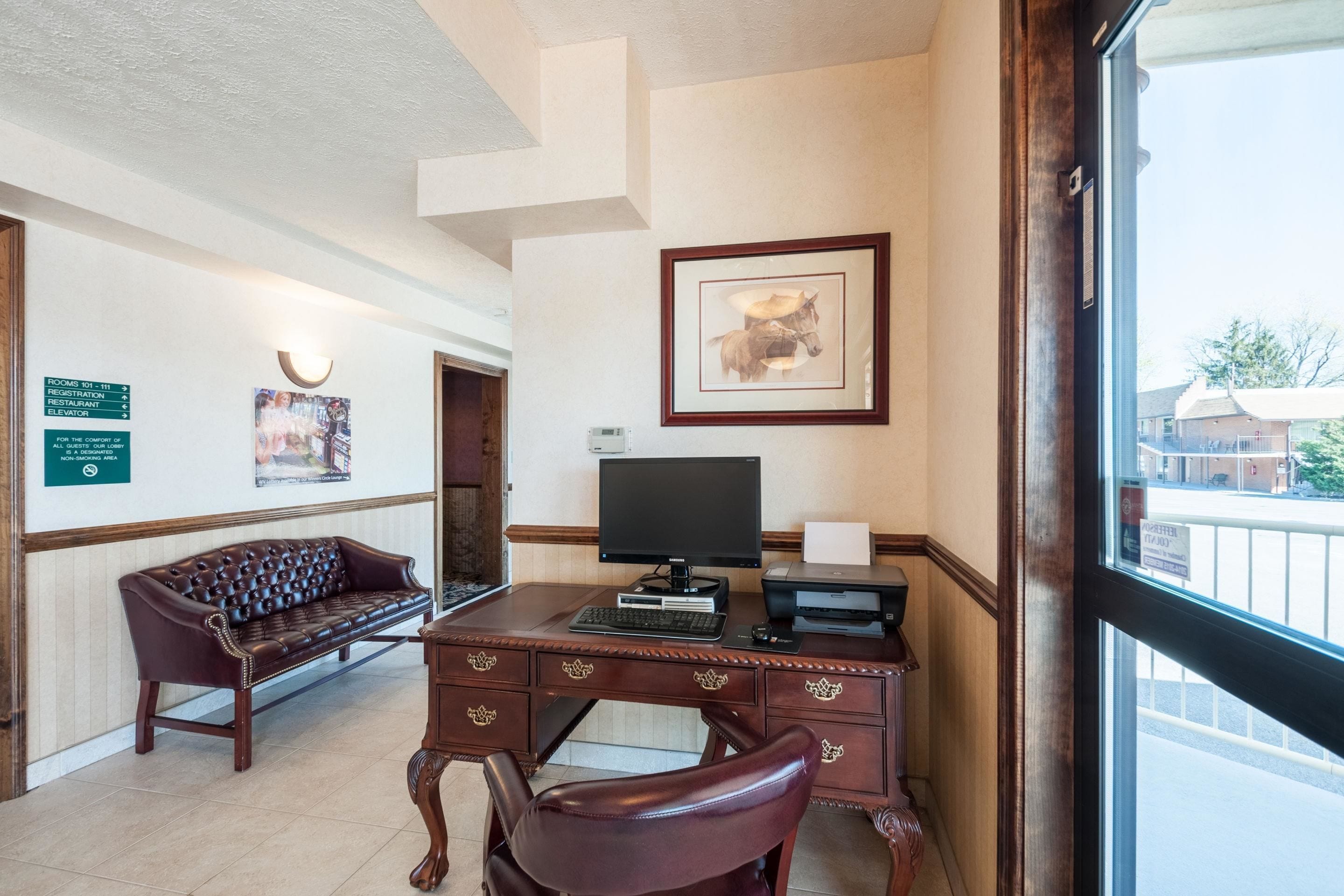 A reception desk with a computer, a framed picture of a dog, a leather sofa, and a sign indicating room numbers.