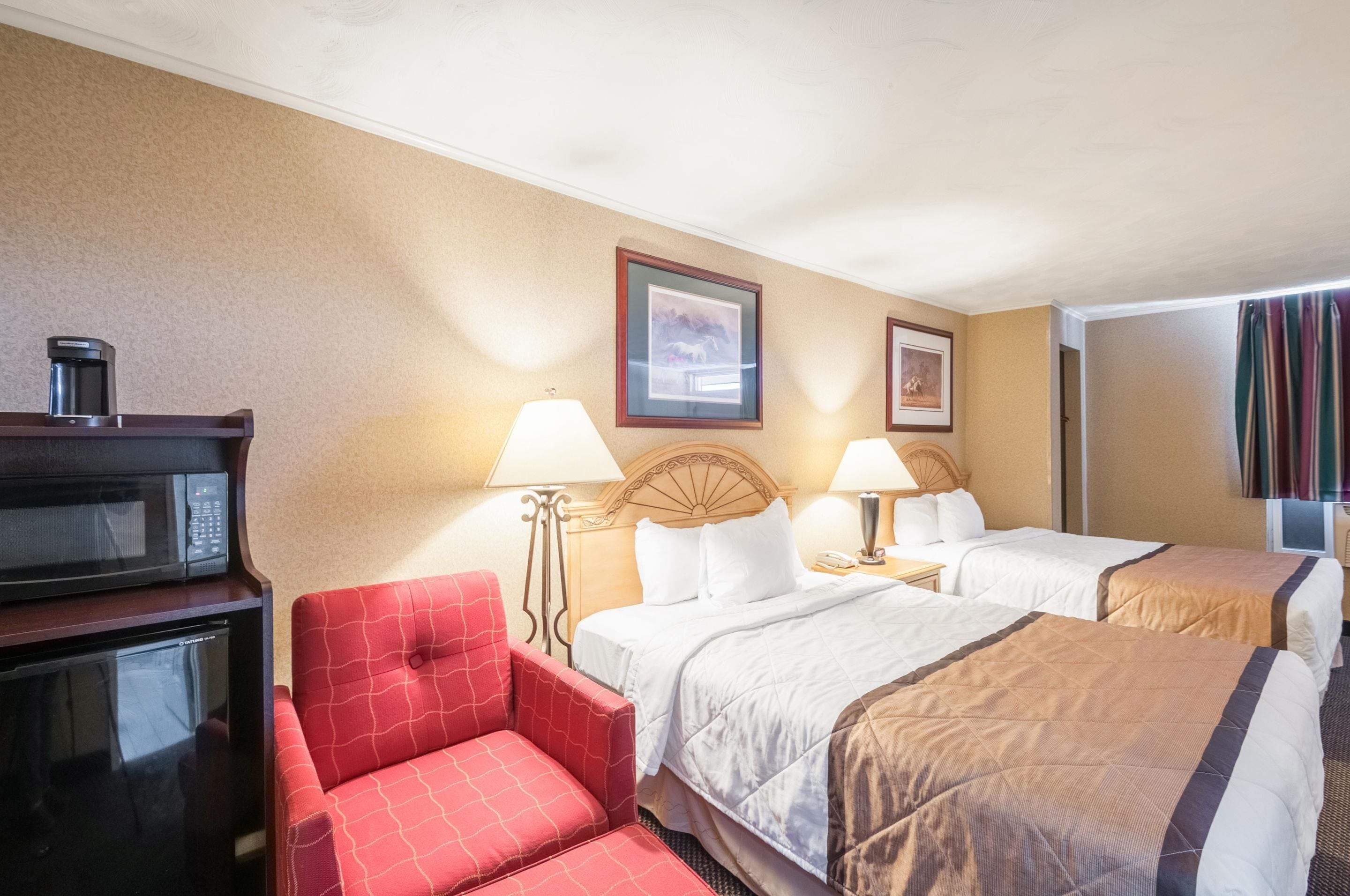 A hotel room with two beds, a red armchair, a microwave, and a coffee maker.