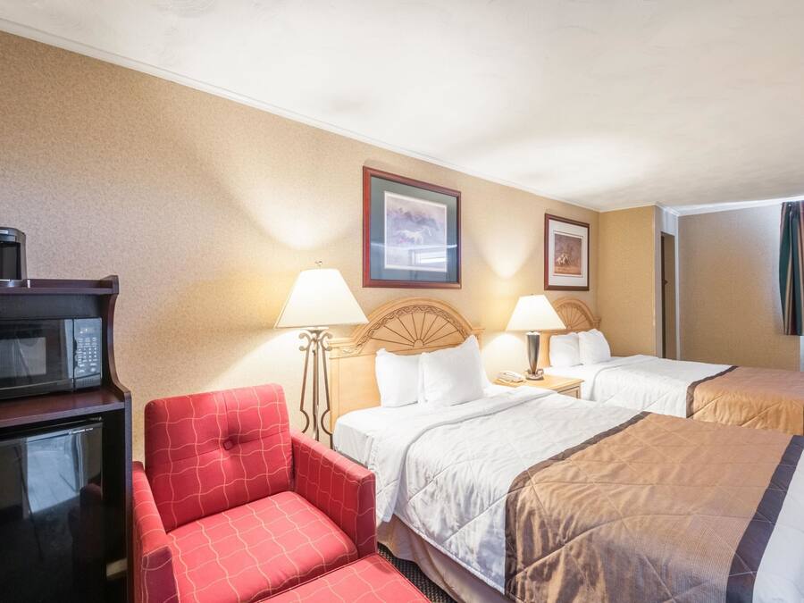 A hotel room with two beds, a red armchair, a microwave, and a coffee maker.