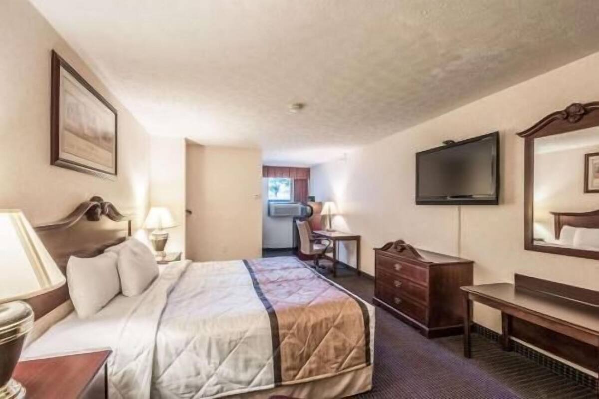 A hotel room with a bed, a desk, a chair, a dresser, a television, and a window.