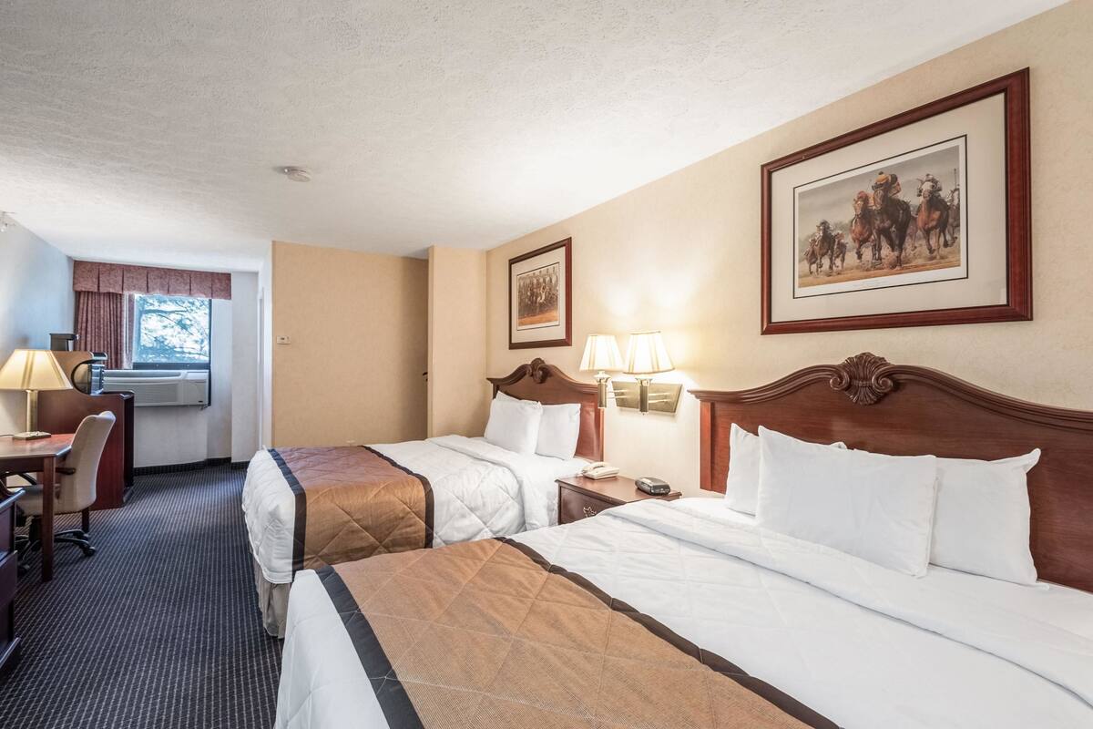 A hotel room with two beds, a desk, a chair, a lamp, and a framed picture on the wall.