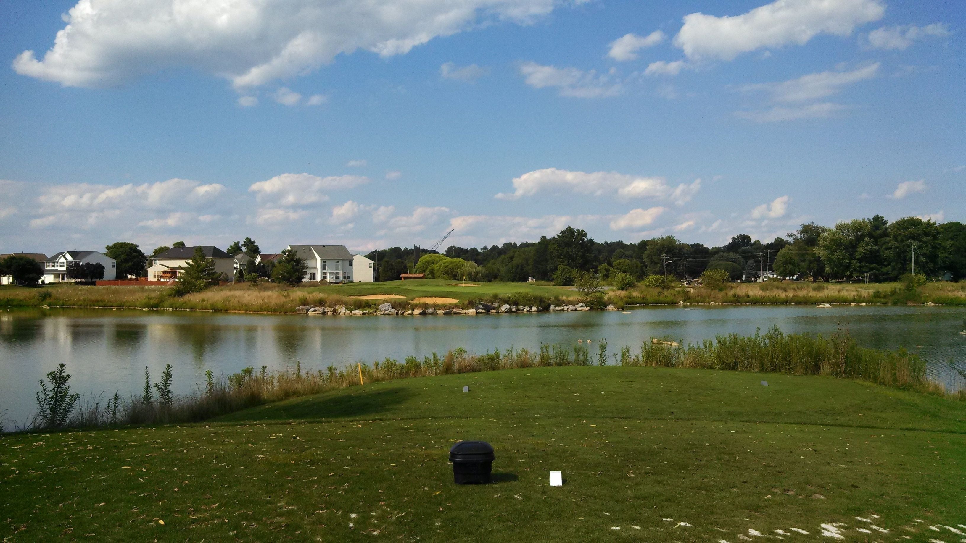 A golf course with a pond, houses in the background, and a crane.