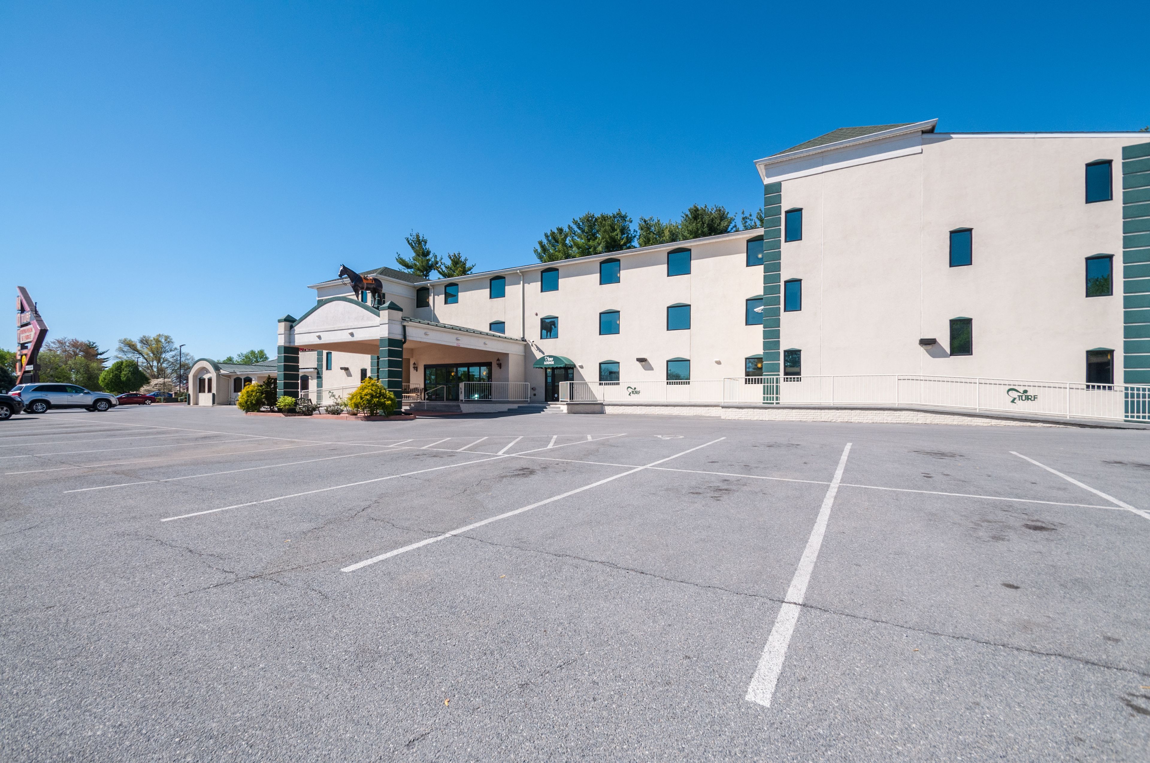 A hotel with a parking lot, a covered entrance, and a building with multiple windows.