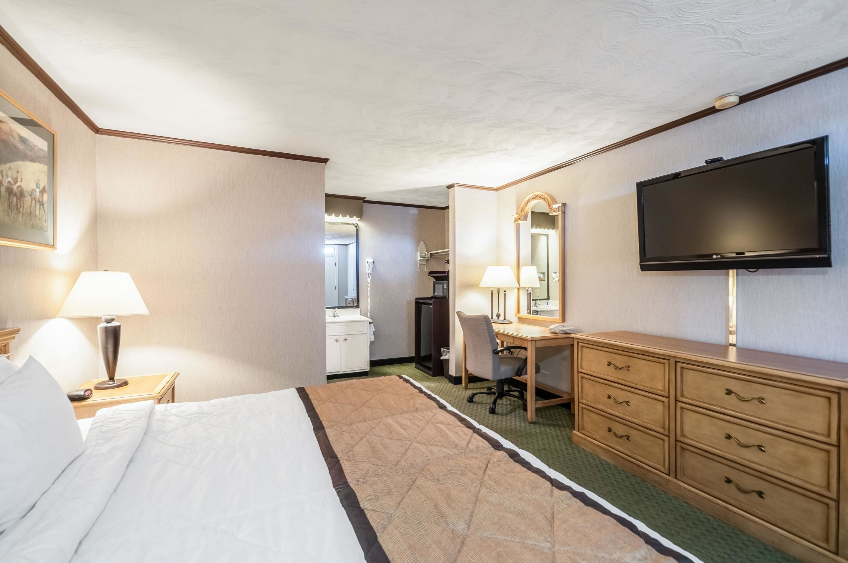 A hotel room with a bed, desk, dresser, TV, and a bathroom in the background.