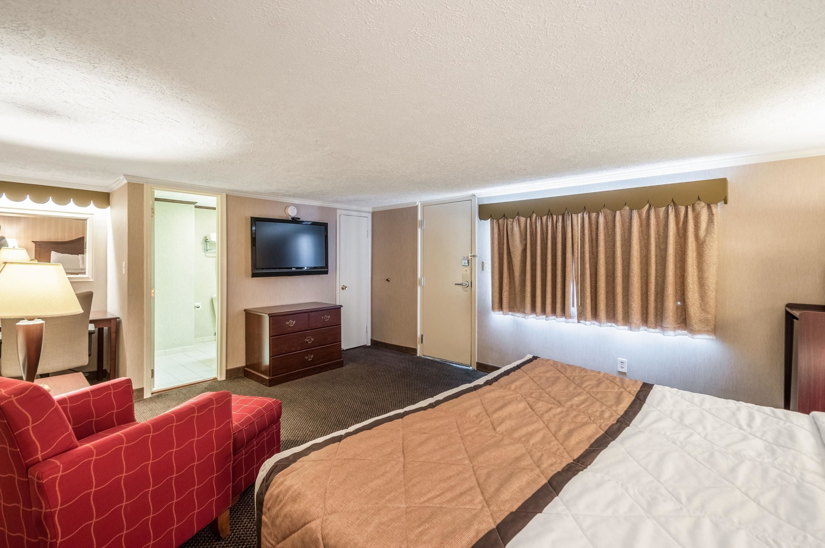 A hotel room with a bed, a TV, a desk, a chair, a dresser, and a window with curtains.